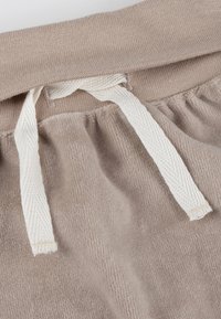 Beige, weicher Stoff mit einer strukturierten Oberfläche, einem elastischen Bund und einer weißen Kordel zum Binden. Auffällige Raffung an der Taille.