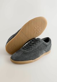 Tenisi gri din suedă, cu vârf rotunjit și design cu șireturi. Prezintă o talpă din cauciuc în nuanță de gumă, cu un model texturat. Stil ușor și casual.