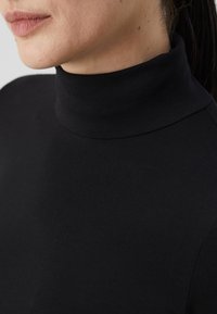 Svart genser med høy hals laget av stretchy stoff, med en tettsittende design og glatt tekstur. Nærbilde av halsområdet uten synlige sømmer.