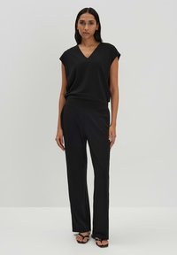 Zwarte V-hals top met korte, cap mouwen, gecombineerd met bijpassende wijde broek. Gladde stof met een zachte textuur, gestyled met platte sandalen.