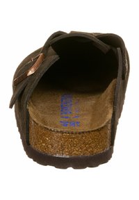 Scarpa slip-on in suede marrone con suola in sughero, esterno nero e dettaglio in fibbia metallica sul lato. Interno liscio con marchio blu.