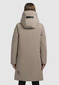 Lange beige jas met een grote capuchon, een gladde textuur en een logo op de achterkant. Heeft een rechte snit en zijzakken.