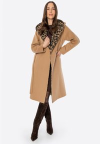 Kurtka w kolorze kamelowym z kołnierzem w leopardzie cętki, długimi rękawami i dopasowaną sylwetką. Noszona na ciemne rajstopy i brązowe kozaki sięgające do kolan.