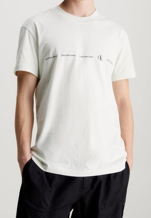 Biała bawełniana koszulka z okrągłym dekoltem i krótkimi rękawami, z powtarzającymi się logo tekstowymi "Calvin Klein Jeans" oraz "CK" w kolorze czarnym.