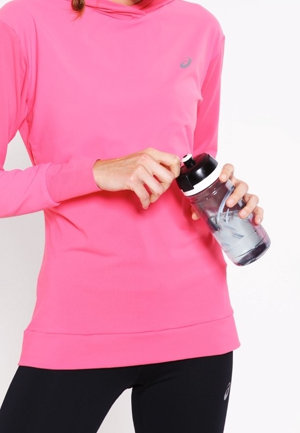 Camiseta deportiva rosa de manga larga con capucha, textura suave y logo reflectante, acompañada de una botella de agua transparente con tapa negra.