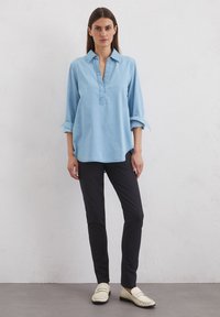 Lichtblauwe, lange mouwen, gekraagde shirt met een pullover ontwerp en subtiel opgerolde mouwen, gecombineerd met zwarte broek en crèmekleurige instapschoenen.