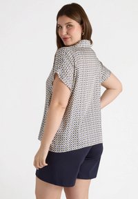 Blusa de manga corta en crema con un patrón geométrico en azul marino y verde. Combinada con pantalones cortos en azul marino oscuro, con un ajuste relajado y una textura suave.
