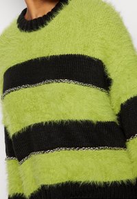Groen en zwart gestreepte trui met een fuzzy textuur en een zachte breiwijze. Zilveren kettingaccenten tussen de strepen voegen detail toe aan het ontwerp.