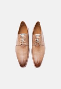 Ζευγάρι καφέ δερμάτινα παπούτσια με μυτερές μύτες και κορδόνια, με διακριτικό υφασμάτινο μοτίβο και επωνησμένους πάτους, σε λευκό φόντο.