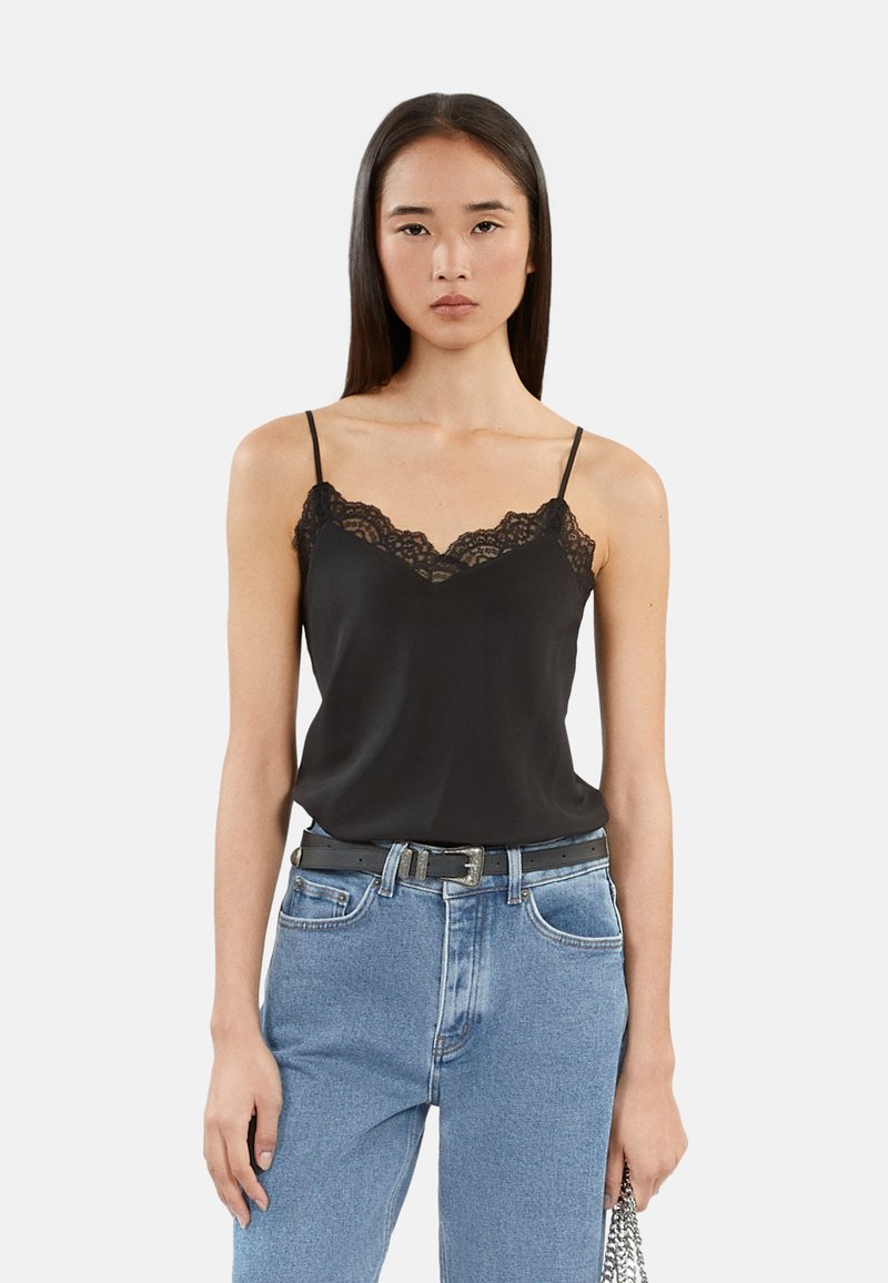 Svart blonde cami med justerbare spaghetti-stropper, med dyp V-hals og en myk tekstur, kombinert med lys blå jeans og et svart belte.