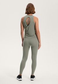 Olive green athletic tank top with a crisscross back design, paired with matching fitted leggings and black athletic shoes.