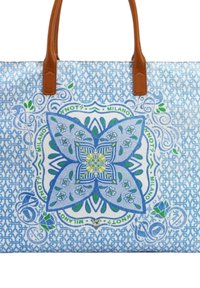 Borsa in tela con motivo floreale blu e bianco, manici in pelle marrone e intricate spirali, che uniscono design geometrici e organici.