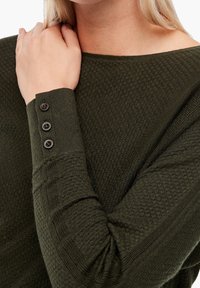 Maglia verde scuro con texture, collo a giro e tre bottoni decorativi nel polsino, che mette in risalto un sottile motivo di tessuto caldo.