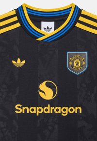Maglia da calcio nera con accenti gialli e blu. Presenta tre strisce gialle sulle spalle, logo Adidas e stemma del Manchester United.
