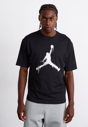 Sort bomulds t-shirt med en stor hvid silhuetgrafik af en basketballspiller i luften. Korte ærmer og rund halsudskæring.
