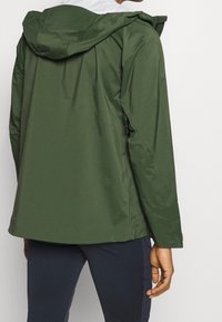 Zielona wodoodporna kurtka z kapturem, o gładkiej fakturze i luźnym kroju. Wyposażona w zasuwane boczne kieszenie oraz regulowane mankiety.