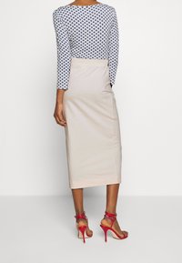 Modrý a bílý dlouhý rukáv s potiskem, kombinovaný s béžovou pouzdrovou sukní a červenými sandály na vysokém podpatku s pásky. Hladké textury po celém outfitu.