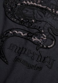 Zwarte stof met zwarte geborduurde letters "chinatown los angeles" en zwarte en grijze kraalversieringen rondom de tekst.