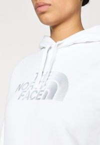 Λευκό φούτερ με κουκούλα από μαλακό ύφασμα με μεγάλο ασημένιο λογότυπο "THE NORTH FACE" στο μπροστινό μέρος και ρυθμιζόμενη κουκούλα με κορδόνια.