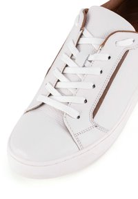 Valge nahast spordiroad tekstuuriga viimistluse, paelte ja pruuni aksessuaariga. Omab ümarat varvast ja minimalistlikku disaini.