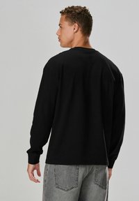 Sort langærmet t-shirt med en afslappet pasform, rund halsudskæring og ribbede manchetter, parret med lysegrå denim jeans.
