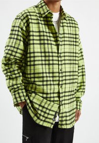 Groen geruite flanel shirt met zwart ruitpatroon, knoopsluiting en een ontspannen pasvorm. Textuur stof met lange mouwen en manchetten.