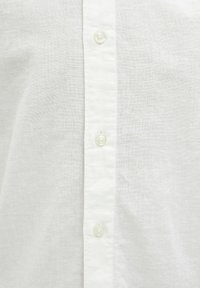 Chemise en lin blanc avec fermeture boutonnée à l'avant ornée de boutons nacrés, texture lisse et tissu léger et respirant.