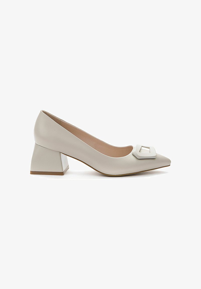 Beige leren pumps met een puntige neus en een opvallende witte vierkante gespdetail, met een blokhak voor stabiliteit en comfort.