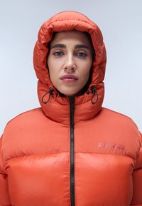 Oranžová péřová bunda se zapínáním na zip, nastavitelnou kapucí a prošívanou texturou. Má logo nášivku na levé horní straně.