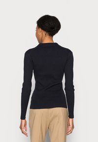 Maglione a maniche lunghe blu navy in maglia a coste, con una silhouette aderente, colletto classico e texture liscia. La vista posteriore mostra dettagli minimi.