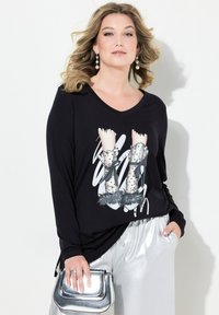 Zwarte lange mouwen top met een V-hals, voorzien van een grafische print van hoge hakken. Gecombineerd met glanzende zilveren broeken en een metallic handtas.