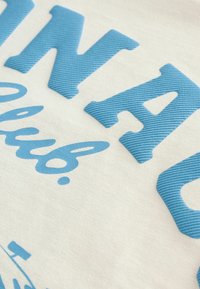 Bavlněná tkanina s modrou žebrovanou typografií, která obsahuje tučné písmo a kurzivní akcenty na světle béžovém pozadí.