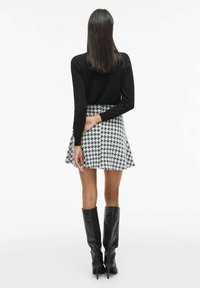 Top nero a maniche lunghe, mini gonna a motivo houndstooth, stivali neri al ginocchio. La vista da dietro mostra una texture liscia e una silhouette aderente.