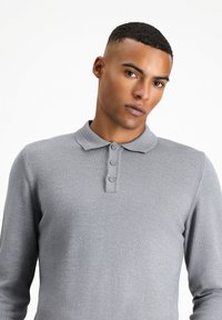 Szara polo z długim rękawem o teksturowanym wykończeniu, z zapięciem na trzy guziki i klasycznym kołnierzykiem. Struktura slim fit.