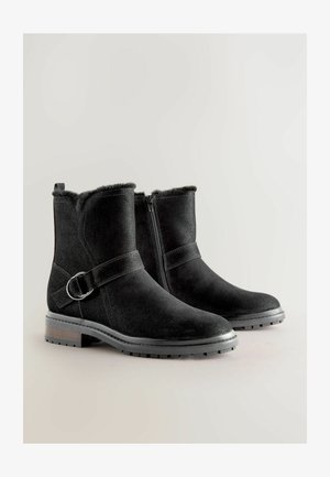 Crne antilop čizmice do gležnjeva sa zatvaranjem na patentni zatvarač, umjetnom krznom oblogom, zaobljenim prstom i dekorativnom kopčom s bočne strane. Izdržljiv teksturiran đon.