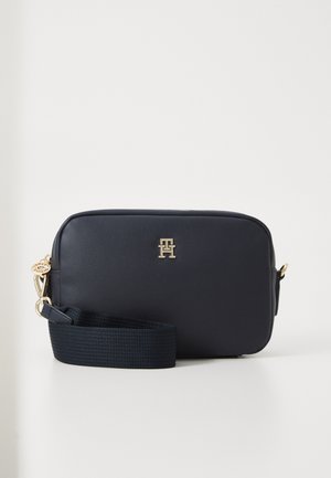 Navyblaue rechteckige Umhängetasche aus glattem Leder mit goldfarbenem Logoakzent und einem strukturierten geflochtenen Tragegurt.