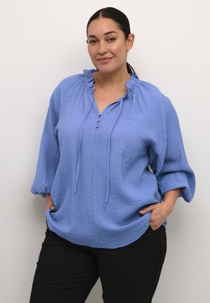 Bluză texturată de culoare albastru deschis cu un guler ondulat, sfori și mâneci până la trei sferturi, asortată cu pantaloni negri.