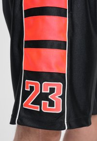 Μαύρο αθλητικό σορτς με κάθετες κόκκινες και μαύρες ρίγες, με τον αριθμό "23" σε έ ντονο κόκκινο και λευκό στο κάτω αριστερό μέρος.