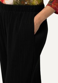 Pantaloni neri plissettati con vita elastica e tasche laterali, caratterizzati da una texture liscia e una silhouette dritta.