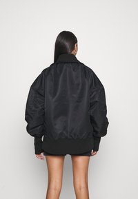 Veste bomber noire avec un extérieur satiné brillant, coupe oversize, poignets et ourlet côtelés, et un col haut. Texture lisse.