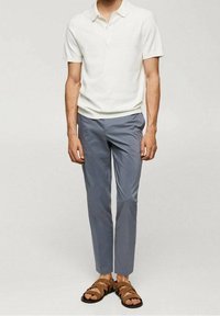 Valkoinen lyhythihainen polo-paita, vaaleansiniset slim fit -housut ja ruskeat sandaalit. Hellä puuvillakangas, rento malli.