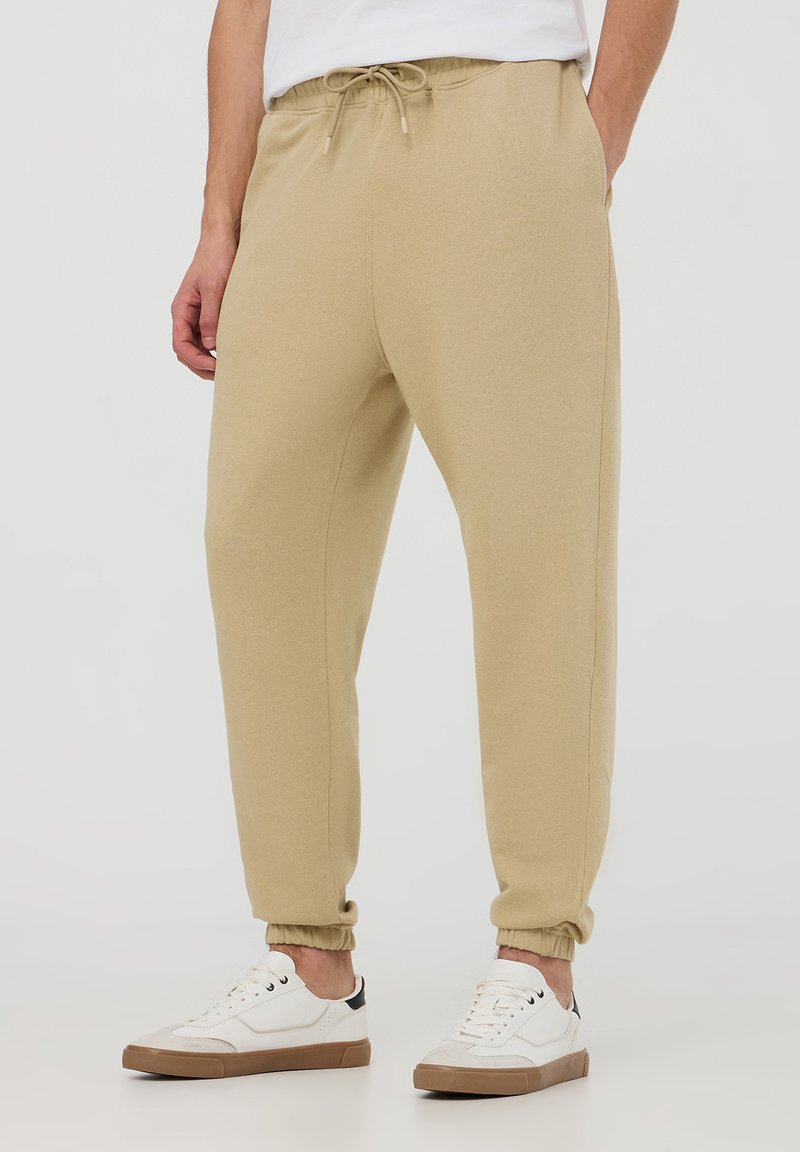 Pantaloni jogger beige realizzati in tessuto morbido, dotati di vita elastica con coulisse, polsini a costine e tasche laterali.