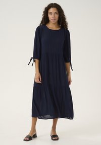 Vestido azul marino, hasta la rodilla, con mangas tres cuartos, diseño en capas y detalles de lazo en las mangas, hecho de una tela ligera.