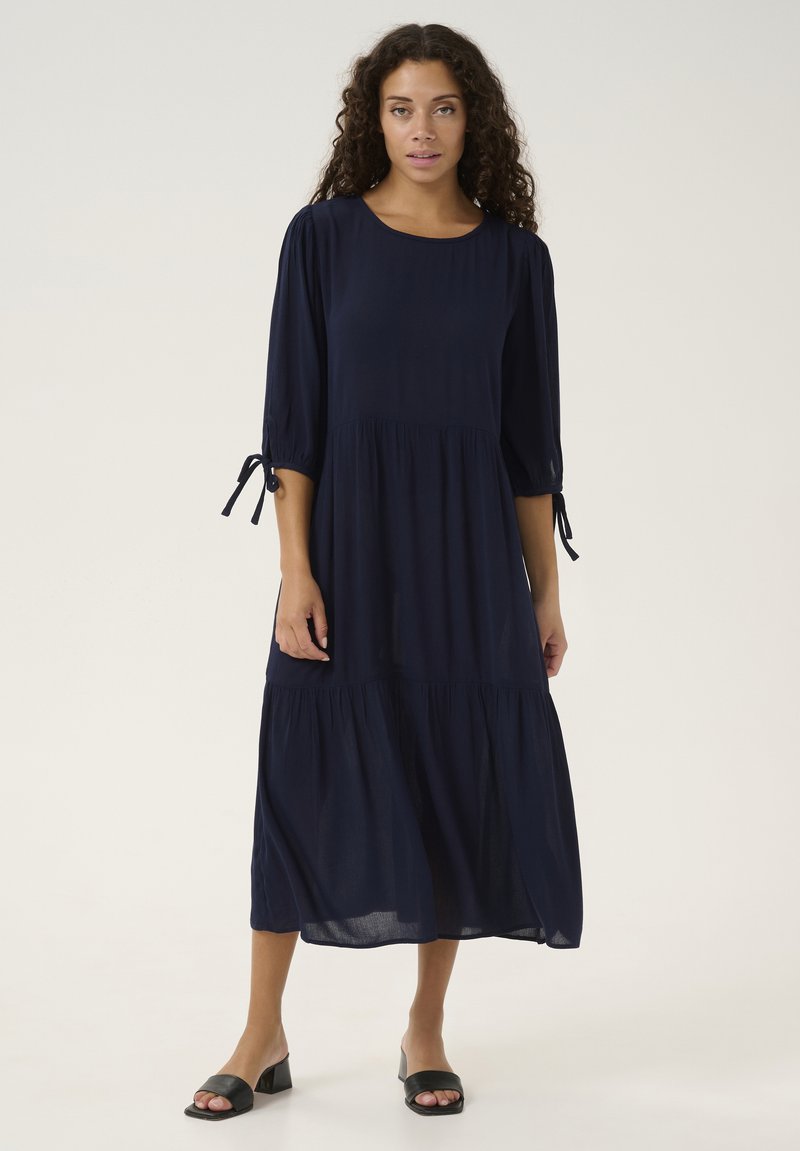 Vestido azul marino, hasta la rodilla, con mangas tres cuartos, diseño en capas y detalles de lazo en las mangas, hecho de una tela ligera.
