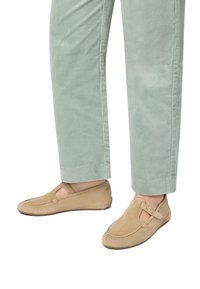 Hellbraune Wildleder-Mokassins mit einem ausgeschnittenen Design und einer seitlichen Schnalle, kombiniert mit hellgrünen Cordhosen.