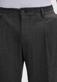 Pantalons noirs texturés avec une fermeture à bouton, une taille élastiquée et un motif tissé subtil, présentant des plis avant pour plus de structure.