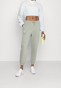 Light green joggers with elastic cuffs, drawstring waist, and white logo. Paired with a cropped light blue sweatshirt and white sneakers.