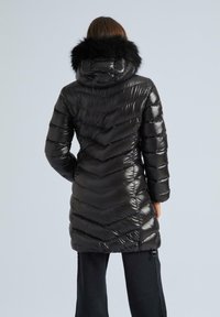 Melna pūkainā jaka ar chevrona quiltu dizainu, noņemamu kažokādas apdari uz kapuces un rāvējslēdzēja sānu kabatām.