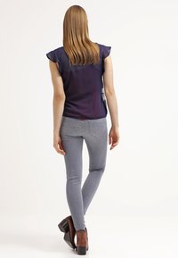 Marinblå topp med fladderärmar, grå smala jeans och bruna klackstövlar. Slät tyg, figurnära design med enkel sömnad och detalj bak.