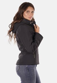 Giacca a cappuccio nera con zip frontale, dotata di tasche laterali e una texture liscia. Il design è aderente e arriva all'anca.